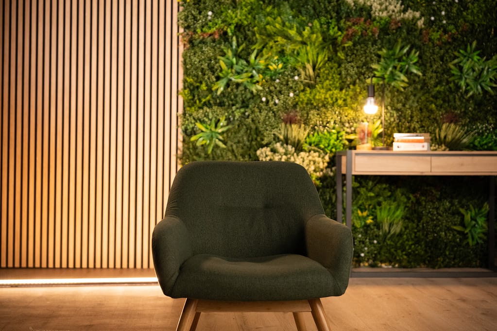 Fauteuil vert en plan rapproché, devant le mur végétal et le panneau en tasseaux bois.