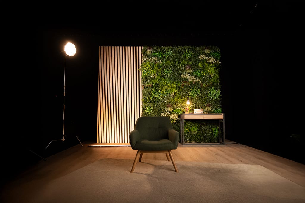 Vue d’ensemble du décor L’Équilibre avec mur végétal, fauteuil vert et bureau bois clair, prêt à tourner.