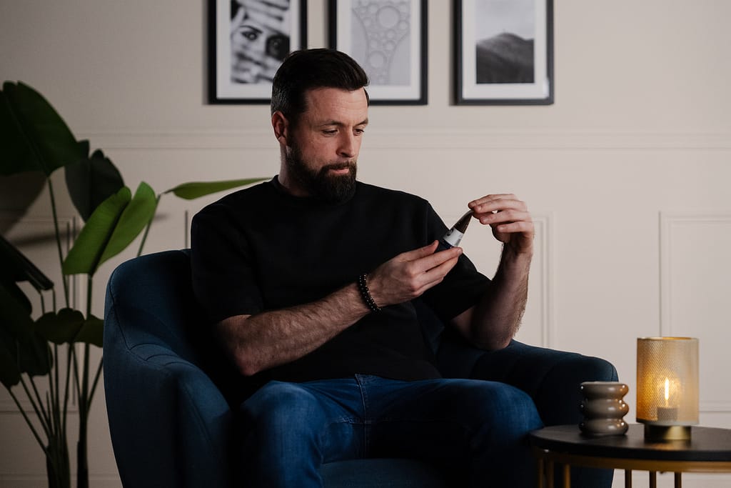 Homme concentré sur un tube de soin visage, installé dans le fauteuil bleu du décor La Parenthèse.