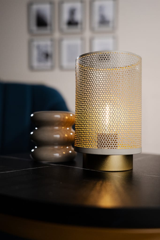 Gros plan sur une bougie allumée dans une lampe en métal perforé, posée sur une table noire du décor La Parenthèse.