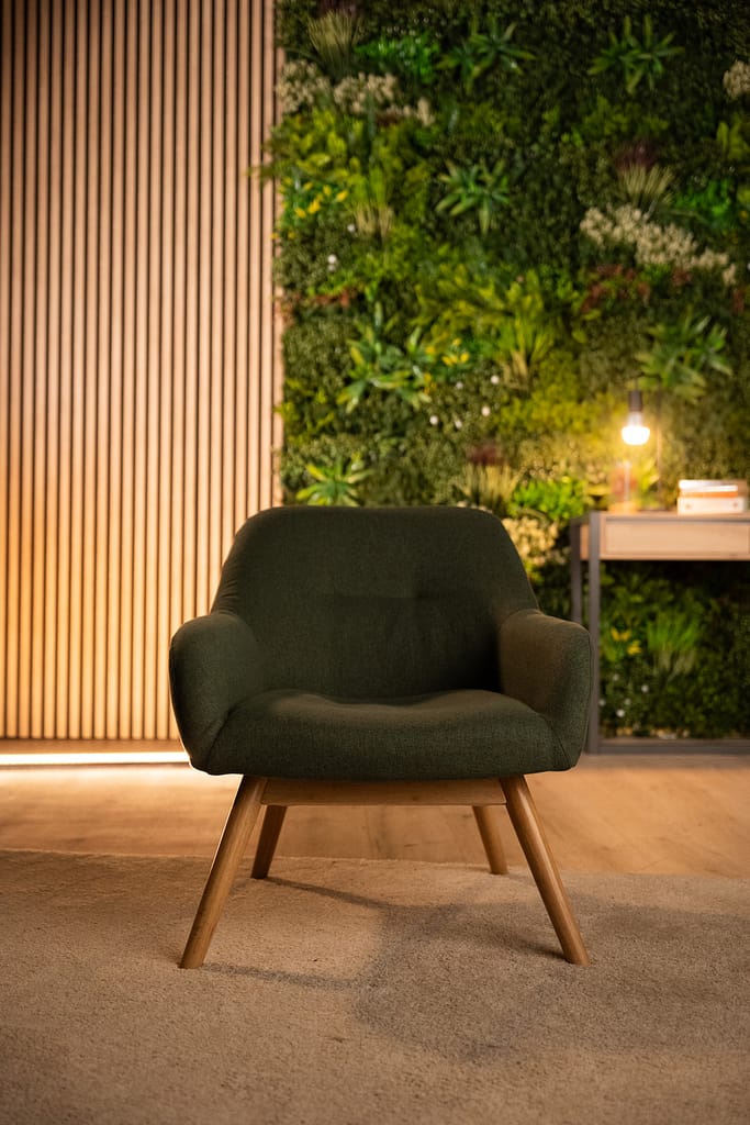 Fauteuil vert en plan rapproché, devant le mur végétal et le panneau en tasseaux bois.