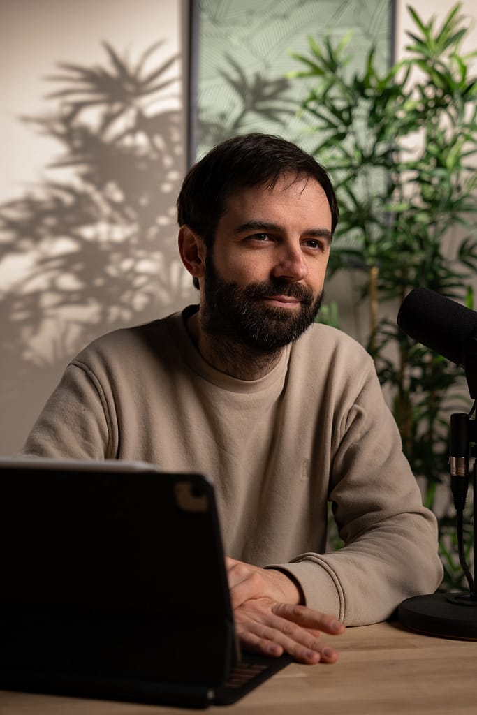 Portrait rapproché d’un homme barbu regardant vers la droite, avec un micro noir en avant-plan.