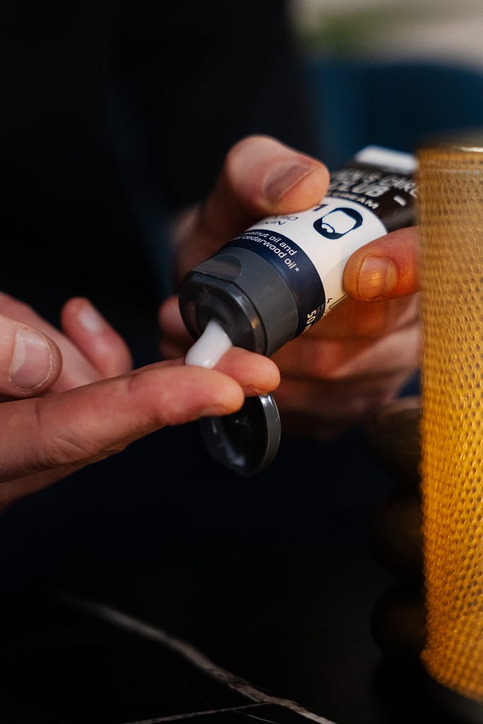 Main d’un homme tenant un tube de cosmétique dans le décor La Parenthèse