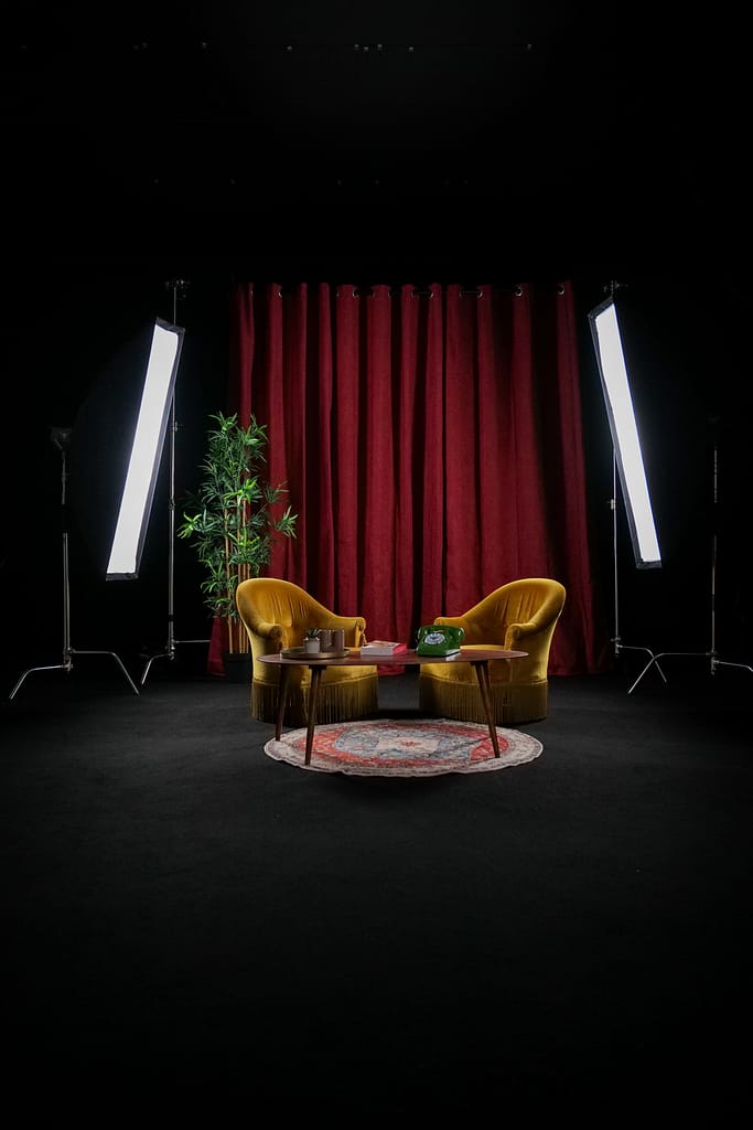 Décor Le Velours avec deux fauteuils jaunes, rideau rouge et lumières de studio