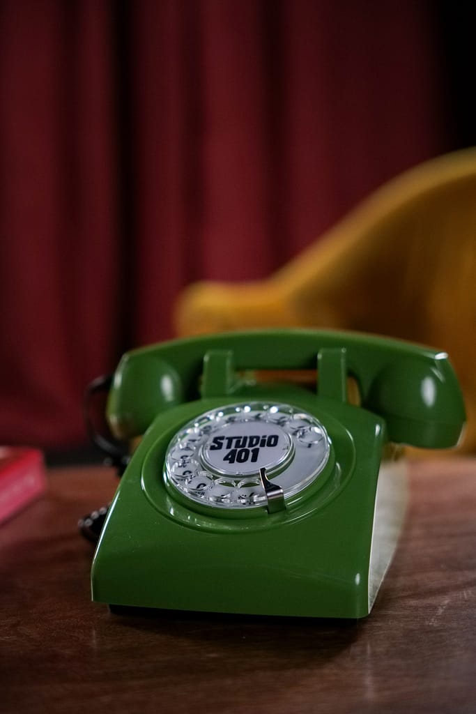 Gros plan sur un téléphone vintage vert marqué Studio 401, posé sur une table en bois